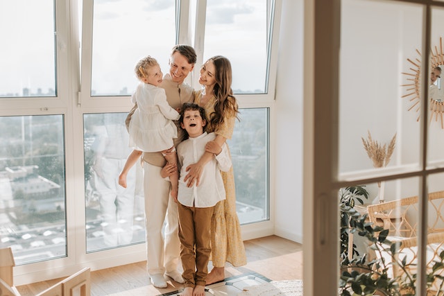 Happy family of four smiling in front of a window